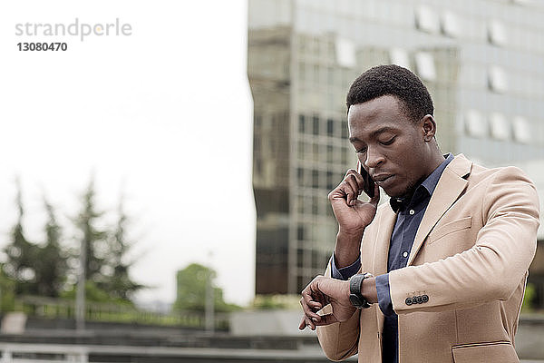Geschäftsmann  der die Uhrzeit überprüft  während er ein Smartphone in der Stadt benutzt