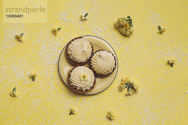 Draufsicht auf Muffins im Teller mit Blumen auf gelbem Hintergrund