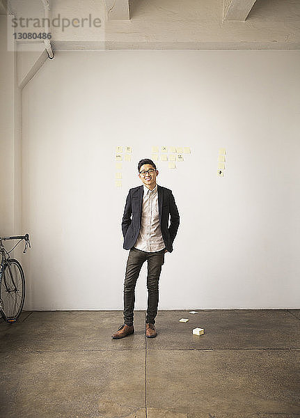 Selbstbewusst lächelnder Geschäftsmann steht im Kreativbüro an der Wand