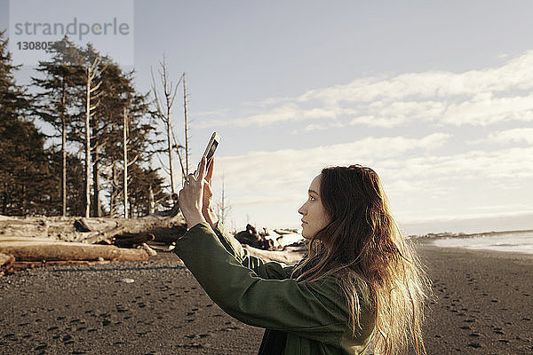 Seitenansicht einer Frau  die mit einem Smartphone am Strand fotografiert