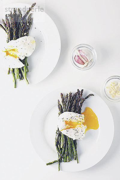 Draufsicht auf Eier mit Spargel  serviert in Tellern mit Knoblauch und Zwiebeln auf weißem Hintergrund