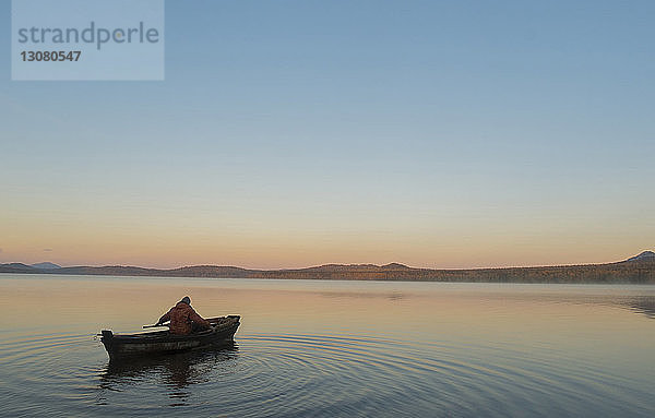 Hochwinkelaufnahme eines Mannes in einem Boot auf dem See vor klarem Himmel bei Sonnenuntergang
