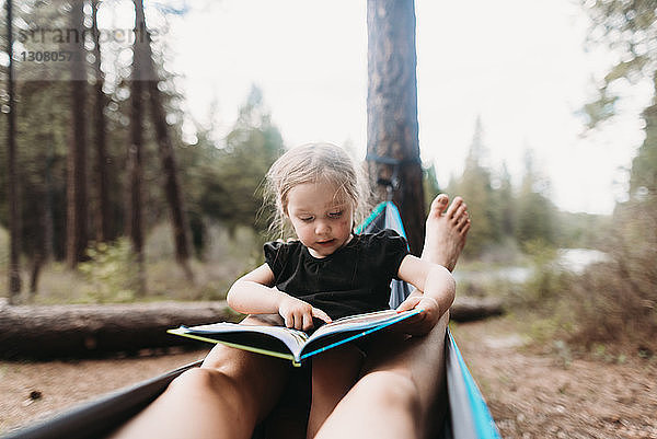 Abgehackte Beine der Mutter um die Tochter  die in der Hängematte auf dem Campingplatz ein Geschichtenbuch liest