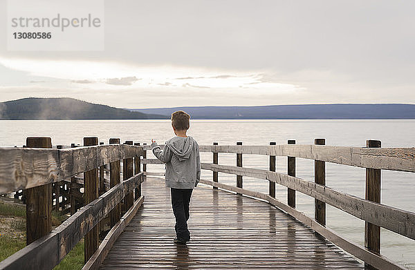 Rückansicht eines Jungen  der auf einem Steg am Meer gegen den Himmel läuft