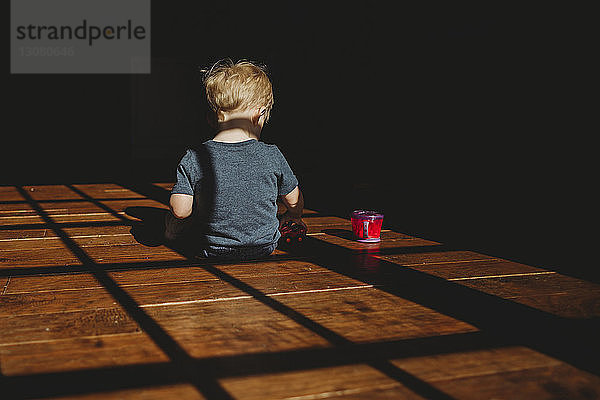 Rückansicht eines kleinen Jungen mit Becher  der zu Hause in der Dunkelkammer sitzt