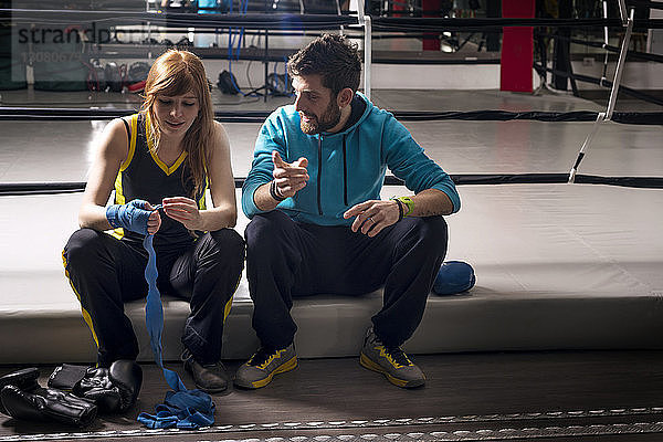 Trainer im Gespräch mit dem Athleten  während er sich nach dem Boxen im Fitnessstudio ausruht