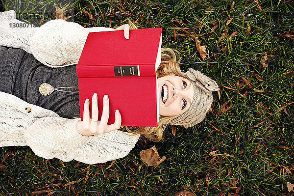 Draufsicht einer glücklichen Frau  die auf einem Grasfeld ein Buch liest