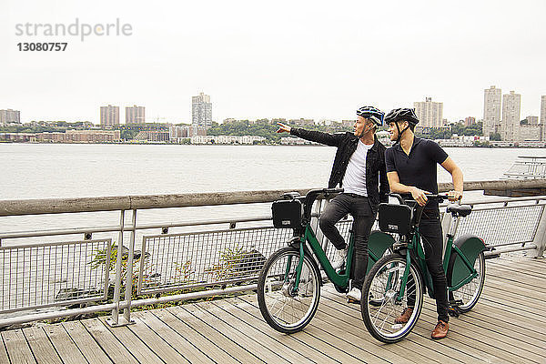 Mann zeigt auf einen Freund und zeigt ihn einem Freund  während er mit dem Fahrrad auf der Promenade steht