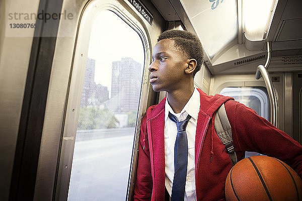 Nachdenklicher Student hält Basketball in der Hand  während er im Zug reist