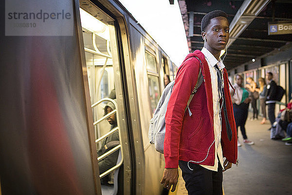 Porträt eines Teenagers  der beim Aussteigen aus dem Zug am Bahnhof Musik hört