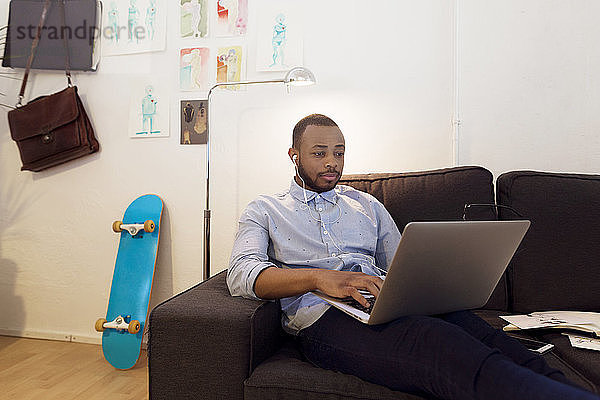 Illustratorin mit Laptop  während sie im Kreativbüro auf dem Sofa sitzt