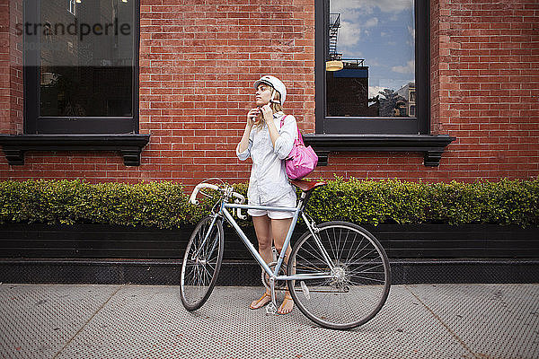 Helmtragende Frau steht mit Fahrrad auf dem Bürgersteig in der Stadt