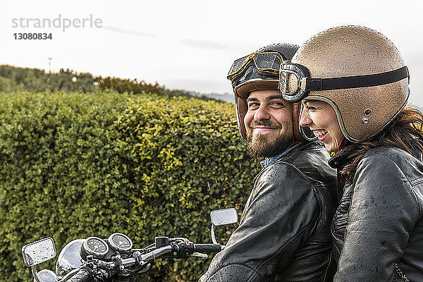 Glückliches Paar unterhält sich auf Motorrad gegen Himmel