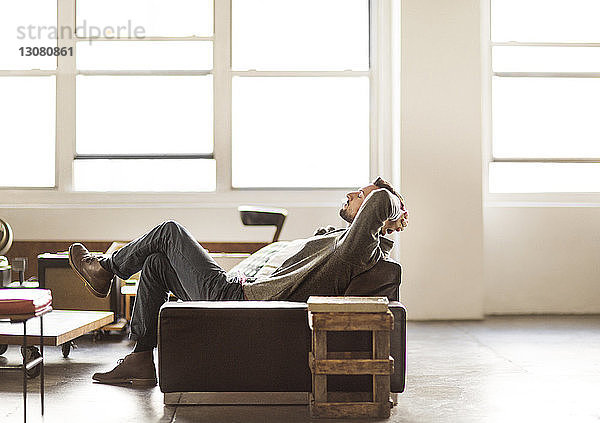 Seitenansicht eines Geschäftsmannes  der sich im hell erleuchteten Kreativbüro auf dem Sofa entspannt