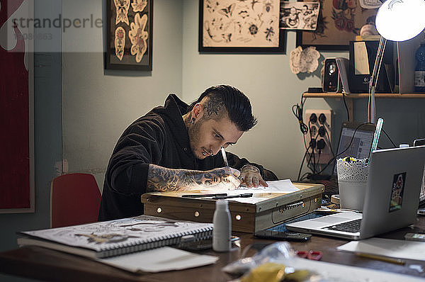 Männlicher Tätowierer beim Zeichnen auf Papier im Atelier