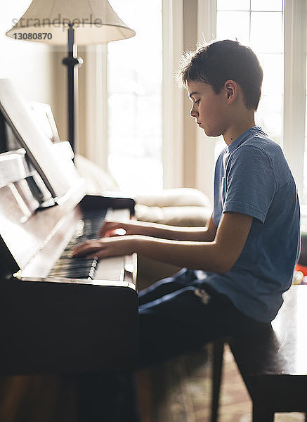 Seitenansicht eines zu Hause sitzenden Jungen  der Klavier spielt