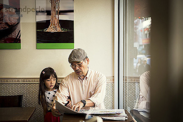 Grossvater zeigt Zeitung  während er mit seiner Enkelin im Restaurant sitzt