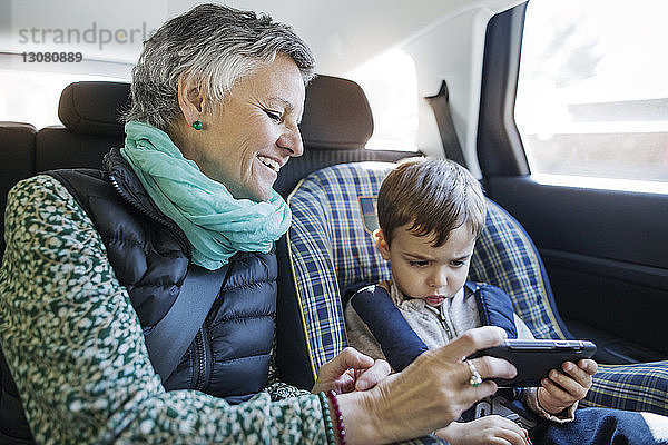 Glückliche ältere Frau mit Smartphone und Enkel im Auto