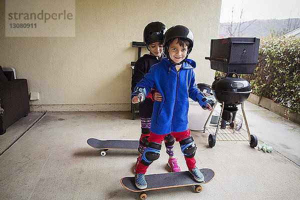 Mädchen assistiert dem Jungen beim Stehen auf dem Skateboard im Hof