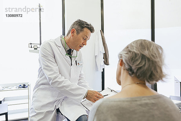 Arzt und ältere Frau schauen auf das Klemmbrett  während sie in einer medizinischen Klinik sitzen