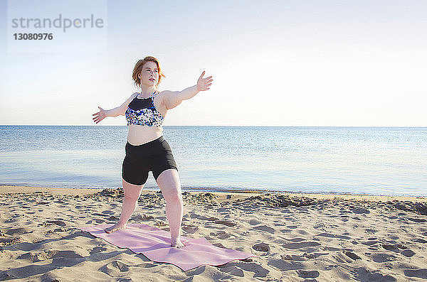 Frau übt Yoga-Pose am Strand bei klarem Himmel