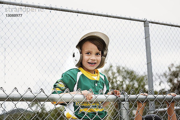 Porträt eines fröhlichen Jungen in Baseball-Uniform vor klarem Himmel