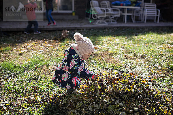 Kleines Mädchen  das im Herbst auf dem Feld im Hof an einem Laubhaufen spielt