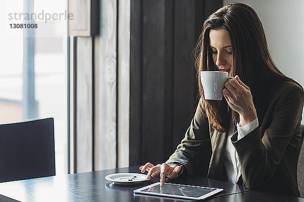 Geschäftsfrau  die Kaffee trinkt  während sie einen Tablet-Computer am Café-Tisch benutzt