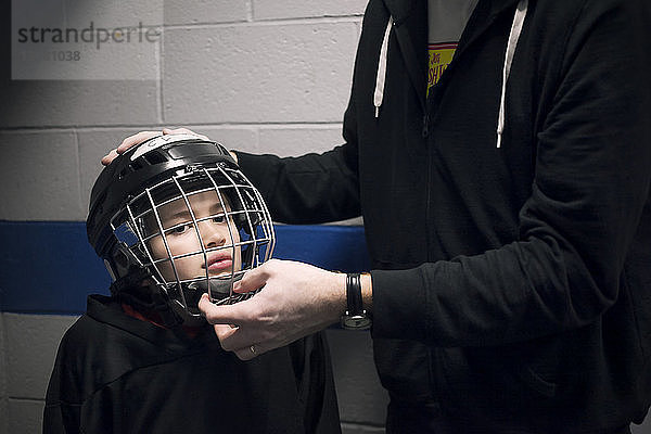 Vater hilft Sohn mit Eishockeyhelm