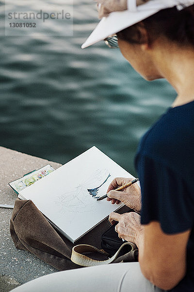 Ausschnitt einer Frau  die auf Papier malt  während sie an einer Stützmauer am Meer ruht