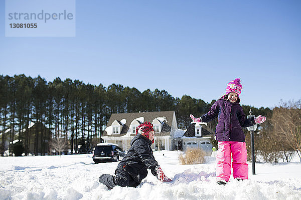 Geschwister spielen mit Schnee auf dem Feld gegen den klaren blauen Himmel