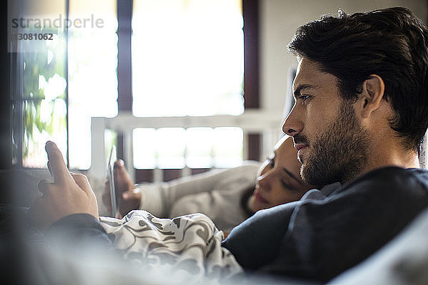 Nahaufnahme eines Paares  das zu Hause im Bett liegt und ein Smartphone benutzt