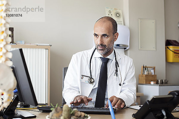 Arzt benutzt Desktop-Computer  während er im Krankenhaus am Tisch sitzt