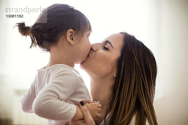 Seitenansicht einer liebenden Mutter  die ihre Tochter zu Hause küsst