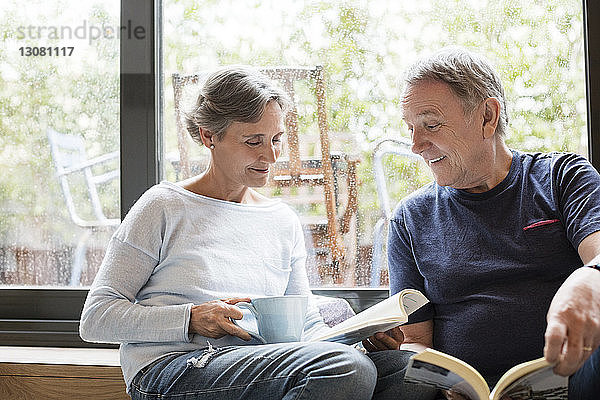 Glückliches älteres Ehepaar liest Bücher  während es zu Hause am Fenster sitzt