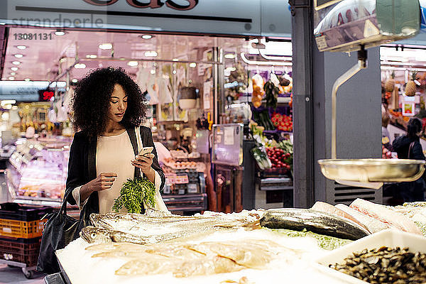 Frau benutzt Mobiltelefon  während sie am Fischmarkt steht