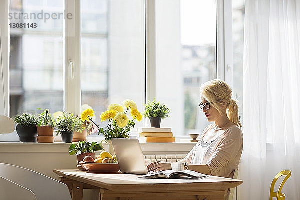Frau benutzt Laptop-Computer  während sie zu Hause am Fenster sitzt
