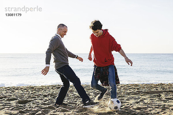 Glückliche Vater und Sohn spielen am Strand bei klarem Himmel Fussball
