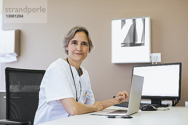Porträt eines leitenden Arztes  der im Krankenhaus an einem Laptop-Computer arbeitet