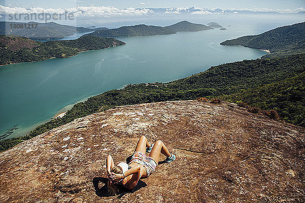Hochwinkelaufnahme einer Frau  die sich am sonnigen Tag auf einem Berg am Meer entspannt