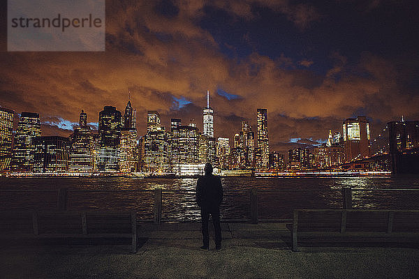 Rückansicht eines Mannes  der während der Nacht auf die beleuchtete Skyline schaut