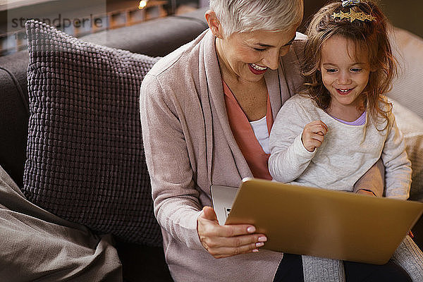 Glückliche Großmutter und Enkelin mit Laptop auf dem Sofa