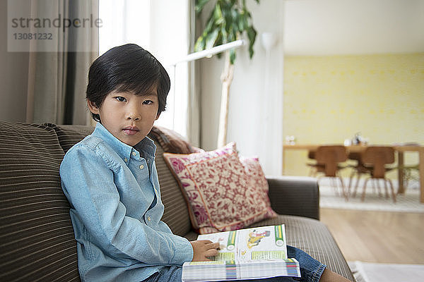 Porträt eines Jungen mit Buch  der zu Hause auf dem Sofa sitzt
