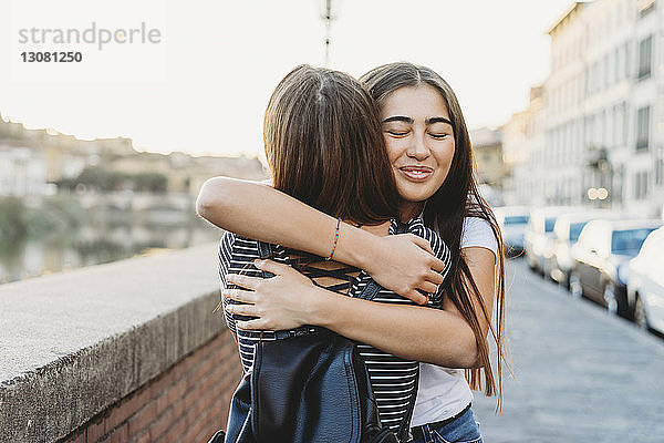 Freunde umarmen sich  während sie auf der Brücke gegen den klaren Himmel in der Stadt stehen