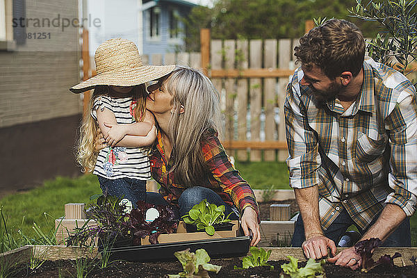 Mann sieht Frau und Tochter bei der Gartenarbeit im Hinterhof