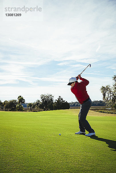 Ein Mann in voller Länge spielt Golf  während er auf dem Feld vor blauem Himmel steht
