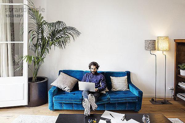 Kreativer Geschäftsmann hört Musik  während er im Büro mit seinem Laptop auf dem Sofa sitzt