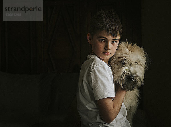 Porträt eines Jungen mit Hund  der zu Hause in der Dunkelkammer steht