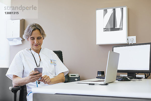 Ältere Ärztin benutzt Mobiltelefon  während sie im Krankenhaus sitzt