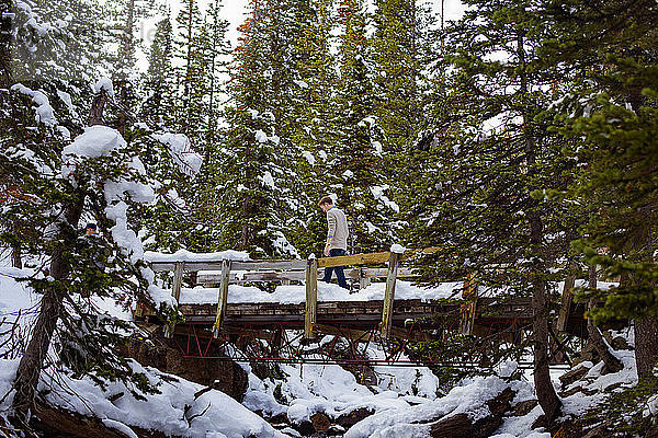Niedrigwinkelansicht eines Mannes  der auf einer schneebedeckten Brücke inmitten von Bäumen geht